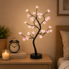 Lampe arbre fleur de cerisier allumée sur une table de chevet à côté d’un réveil