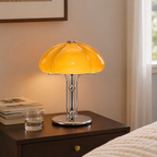 Lampe champignon orange allumée sur une table de chevet en bois dans une chambre