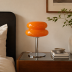 Lampe en verre orange allumée sur une table de chevet à côté d’un lit