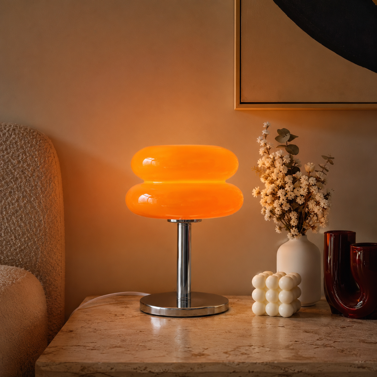 Lampe en verre orange allumée sur un meuble en bois avec des fleurs séchées