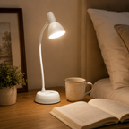 Lampe à col flexible allumée sur une table de nuit avec une tasse et un livre ouvert.