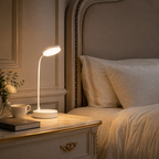 Lampe flexible allumée sur une table de nuit avec une tasse, à côté d'un lit fait.