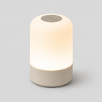 Lampe cylindrique allumée vue de trois quarts sur fond gris, diffusion lumineuse à 360°.