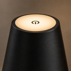 Gros plan de l'abat-jour noir allumé en lumière chaude, bouton tactile visible au sommet.
