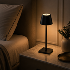 Chambre tamisée le soir, lampe noire allumée diffusant une lueur chaude vers le lit.