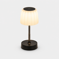 Lampe à abat-jour plissé blanc allumée, tige métallique et base noire, sur fond neutre.