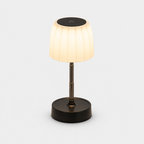 Lampe à abat-jour plissé blanc allumée, tige métallique et base noire, sur fond neutre.