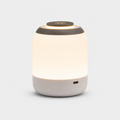 Lampe cylindrique allumée à diffuseur blanc et dessus gris, port de recharge visible.