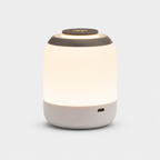 Lampe cylindrique allumée à diffuseur blanc et dessus gris, port de recharge visible.